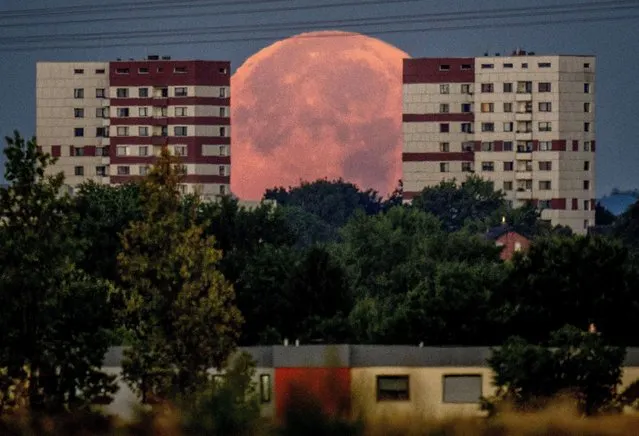The full moon sets behind apartment houses in the outskirts of Frankfurt, Germany, early Friday, August 12, 2022. (Photo by Michael Probst/AP Photo)
