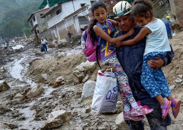A firefighter holds two girls in an area where several homes were destroyed by a mudslide caused by heavy rains in Valle del Mocoties community, municipality of Tovar, Merida state, Venezuela on August 26, 2021. The death toll from heavy rains that triggered mudslides and floods in western Venezuela has risen to 20, local authorities said Wednesday, with 17 other people missing. Nine states are in an “emergency” situation and more than 54,000 people have been affected by the downpours, Interior Minister Remigio Ceballos told state television. (Photo by Miguel Zambrano/AFP Photo)
