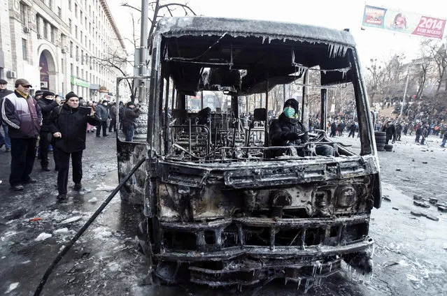 A pro-European integration protester sits in a burnt police bus after a rally near government administration buildings in Kiev January 20, 2014. (Photo by Vasily Fedosenko/Reuters)
