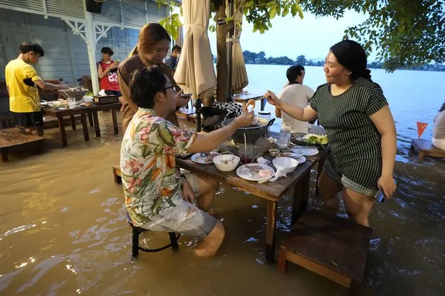 Customers of the riverside Chaopraya Antique Café enjoy themselves despite the extraordinary high water levels in the Chao Phraya River in Nonthaburi, near Bangkok, Thailand, Thursday, October 7, 2021. The flood-hit restaurant has become an unlikely dining hotspot after fun-loving foodies began flocking to its water-logged deck to eat amid the lapping tide. Now, instead of empty chairs and vacant tables the “Chaopraya Antique Café” is as full as ever, offering an experience the canny owner has re-branded as “hot-pot surfing”. (Photo by Sakchai Lalit/AP Photo)