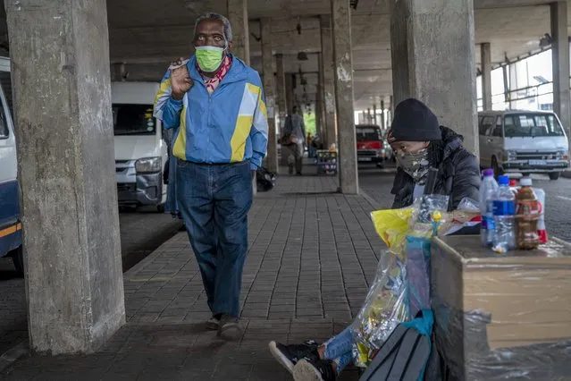 A woman selling snacks, sits at the Baragwanath taxi rank in Soweto, South Africa, Thursday December 2, 2021. South Africa launched an accelerated vaccination campaign to combat a dramatic rise in confirmed cases of COVID-19 a week after the omicron variant was detected in the country. (Photo by Jerome Delay/AP Photo)