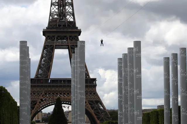A participant rides a zipline tied from the second floor of the Eiffel Tower, 115 metres above the Champ de Mars gardens along an 800-meters long cable, as part of a free event in Paris, France, Tuesday, May 28, 2019. (Photo by Francois Mori/AP Photo)