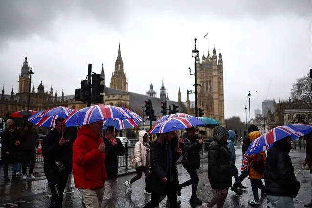 Pedestrians shelter from the rain under Union flag umbrellas as they pass the Elizabeth Tower, commonly known by the name of the clock's bell, “Big Ben”, at the Palace of Westminster, home to the Houses of Parliament, in London on February 22, 2024. (Photo by Henry Nicholls/AFP Photo)