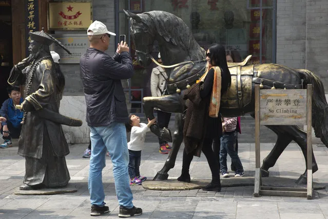 In this Wednesday, April 13, 2016 photo, a woman poses for photos near bronze sculptures along a retail street in Beijing. (Photo by Ng Han Guan/AP Photo)