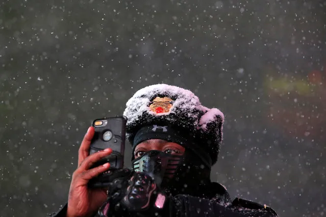 Times Square Public Safety Sergeant Baldwin Davis captures falling snow with his cellular device in Times Square in Manhattan, New York, U.S., March 14, 2017. (Photo by Andrew Kelly/Reuters)