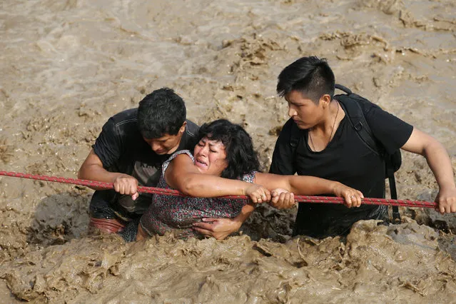 A woman is assisted while crossing a flooded street after the Huayco river overflooded its banks sending torrents of mud and water rushing through the streets in Huachipa, Peru, March 17, 2017. (Photo by Guadalupe Pardo/Reuters)