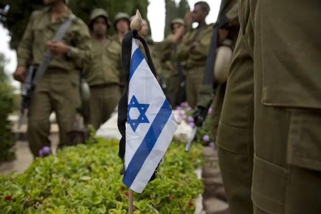 Israeli soldiers stand next to a small flag with a black ribbon placed on a grave of a fallen soldier on the eve of memorial Day in Kiryat Shaul military cemetery in Tel Aviv, Israel, Tuesday, May 10, 2016. (Photo by Ariel Schalit/AP Photo)