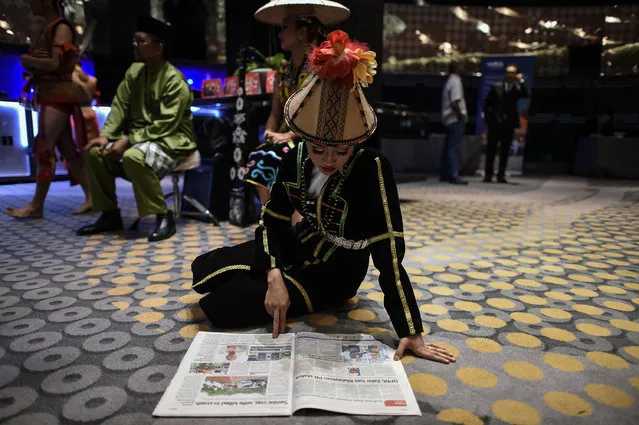 A Malaysian dancer in Sabah tribal costumes reads a newspaper on the floor as Malaysia's Prime Minister Najib Razak delivers his keynote address at the Publish Asia media industry conference in Kuala Lumpur on April 19, 2017. (Photo by Mohd Rasfan/AFP Photo)