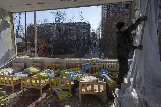 A man removes a destroyed curtain inside a school damaged among other residential buildings in Kyiv, Ukraine, Friday, March 18, 2022. Russian forces pressed their assault on Ukrainian cities Friday, with new missile strikes and shelling on the edges of the capital Kyiv and the western city of Lviv, as world leaders pushed for an investigation of the Kremlin's repeated attacks on civilian targets, including schools, hospitals and residential areas. (Photo by Rodrigo Abd/AP Photo)