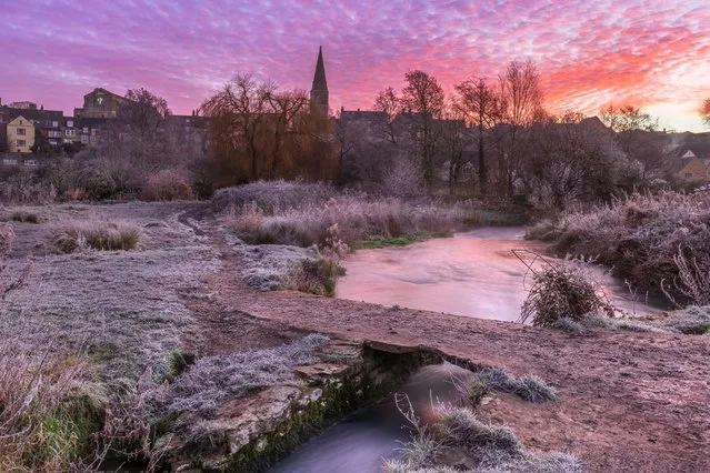 After a heavy overnight frost, the dawn sky turns pink over the ancient clapper bridge that leads towards the hillside market town in Wiltshire, England on January 12, 2022 (Photo by Terry Mathews/Alamy Live News)