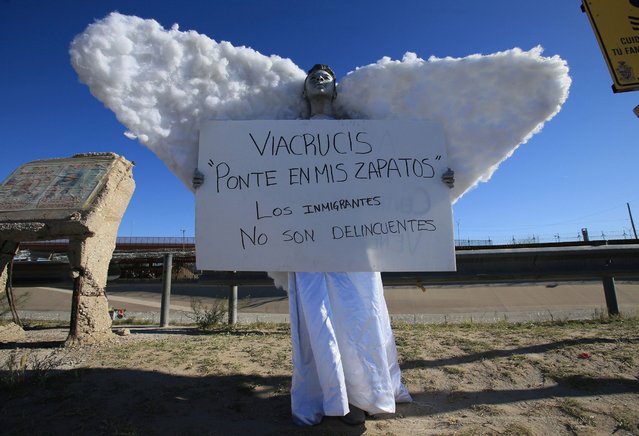 A Young man dressed as an angel holds a sign that reads in Spanish “Via Crucis Be in my shoes. Immigrants are not criminals”, during a Stations of the Cross on Palm Sunday by the Rio Grande near Ciudad Juarez, Mexico, Sunday, April 2, 2023. The Via Crucis took place just a few meters from the border fence that separates Mexico and the United States. (Photo by Christian Chavez/AP Photo)