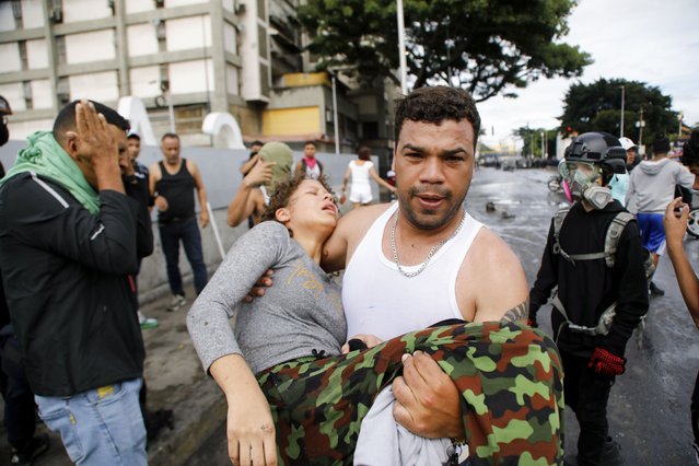 A man carries a protester affected by tear gas thrown by police during demonstrations against the official election results declaring President Nicolas Maduro's reelection, the day after the vote, in the Caria neighborhood of Caracas, Venezuela, Monday, July 29, 2024. (Photo by Cristian Hernandez/AP Photo)