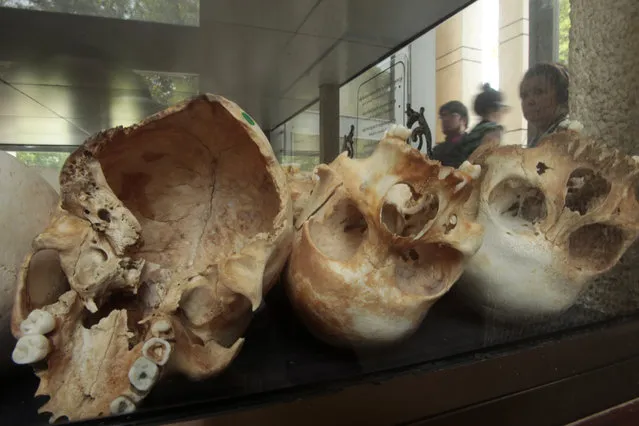 Visitors watch human skulls and bones of victims in Khmer Rouge regime on display at Choeung Ek memorial on the outskirts of Phnom Penh, Cambodia, Wednesday, June 14, 2017. Prosecutors at the trial in Cambodia of the surviving top leaders of the former Khmer Rouge regime have begun summing up their case, declaring that, despite the defendants’ denials, the evidence clearly showed they knew of the suffering and deaths of their countrymen. An estimated 1.7 million Cambodians died during communist group’s bloody reign in the late 1970s. (Photo by Heng Sinith/AP Photo)