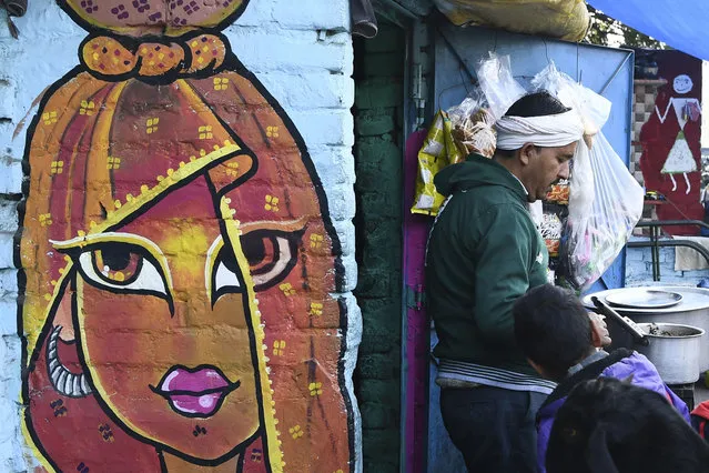 A vendor waits for customers while standing near a mural painted by artists from “Delhi Street Art” group at the Raghubir Nagar slum in New Delhi on December 2, 2019. (Photo by Sajjad Hussain/AFP Photo)