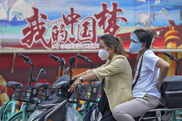 Women wearing face masks sit on a scooter near a poster promoting the “China Dream” in Beijing, Monday, June 20, 2022. (Photo by Andy Wong/AP Photo)