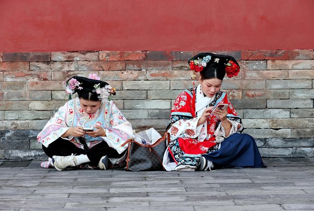 Two young women in traditional dress check their phones in Tiantan Park in Beijing, China on October 24, 2024. (Photo by Rex Features/Shutterstock)