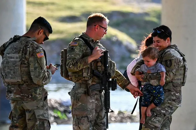 US Border Patrol and National Guard troops play with a migrant child as a group of migrants are apprehended in Eagle Pass, Texas, near the border with Mexico on June 30, 2022. Every year, tens of thousands of migrants fleeing violence or poverty in Central and South America attempt to cross the border into the United States in pursuit of the American dream. Many never make it. On June 27, around 53 migrants were found dead in and around a truck abandoned in sweltering heat near the Texas city of San Antonio, in one of the worst disasters on the illegal migrant trail. (Photo by Chandan Khanna/AFP Photo)