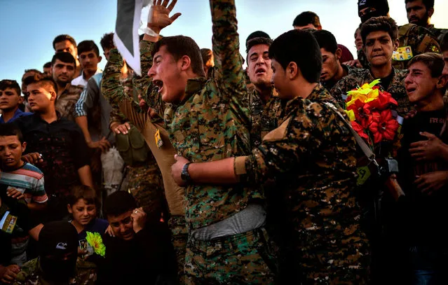 A picture taken on October 14, 2017 in the Kurdish town of Kobane in northern Syria shows people and members of the Kurdish People' s Protection Units (YPG) mourning during the funeral of a Kurdish fighter, who was killed in clashes against Islamic State (IS) group fighters in the city of Deir Ezzor Syrian fighters backed by US special forces are battling to clear the last remaining IS jihadists holed up in their crumbling stronghold of Raqa. (Photo by Bulent Kilic/AFP Photo)