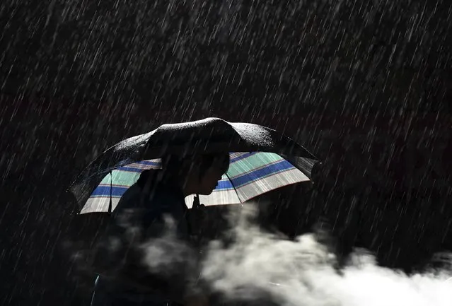 A woman holds an umbrella as she cooks in the rain at the earthquake zone of Longtoushan town, Ludian county, Zhaotong, Yunnan province, August 7, 2014. The earthquake in China on the weekend triggered landslides that have blocked rivers and created rapidly growing bodies of water that could unleash more destruction on survivors of the disaster that killed 615 people, state media reported. (Photo by Reuters/China Daily)