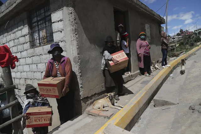 People wearing face masks hold food boxes distributed by the government during a lockdown to contain the spread of COVID-19 in a poor area on the outskirts of Quito, Ecuador, Wednesday, May 27, 2020. (Photo by Dolores Ochoa/AP Photo)