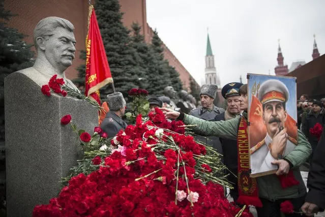 A woman holding a portrait of Stalin places flowers near the monument signifying Joseph Stalin's grave near the Kremlin wall marking the anniversary of Stalin's birth in Moscow's Red Square, Russia, Thursday, December 21, 2017. (Photo by Alexander Zemlianichenko/AP Photo)