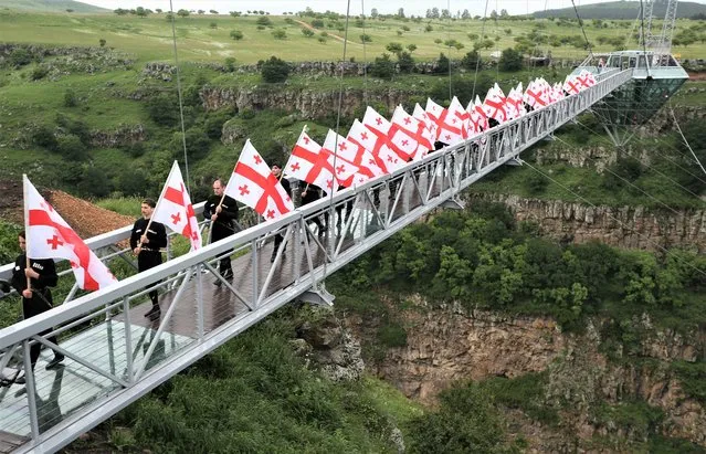 People carry Georgian flags as they walk on the glass bridge over Dashbashi Canyon during the opening ceremony outside the town of Tsalka, Georgia on June 14, 2022. (Photo by Irakli Gedenidze/Reuters)