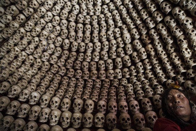 An ethnic Tibetan woman from Kham area wearing traditional amber headwear looks at fake human skulls placed inside a room at the site for sky burials near the Larung valley located some 3700 to 4000 metres above the sea level in Sertar county, Garze Tibetan Autonomous Prefecture, Sichuan province, China October 31, 2015. (Photo by Damir Sagolj/Reuters)