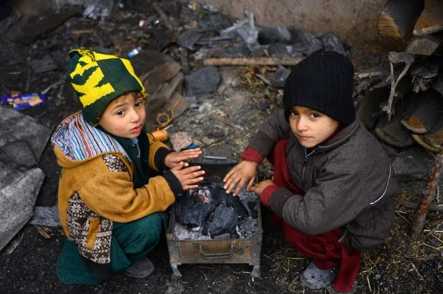 Children warm up themselves around a charcoal fire, in Herat on November 22, 2020. (Photo by Hoshang Hashimi/AFP Photo)