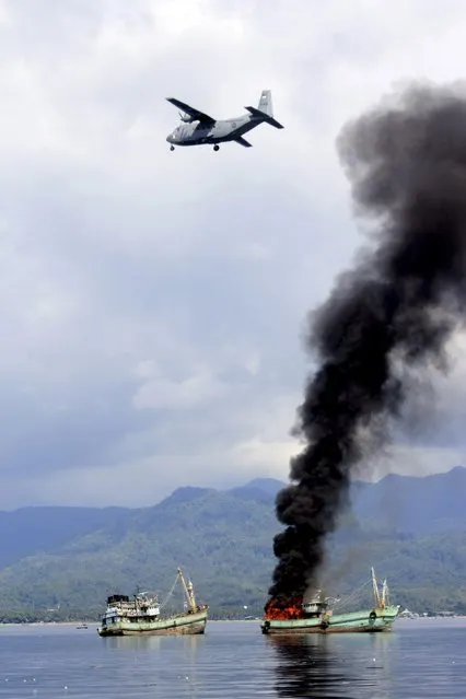 An Indonesian Navy plane passes over two foreign flagged fishing boats registered in Papua New Guinea as they are being destroyed by the navy after were seized earlier for supposedly illegal fishing off the coast of Ambon, Maluku December 21, 2014 in this photo taken by Antara Foto. (Photo by Izaac Mulyawan/Reuters/Antara Foto)