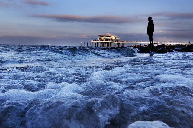 A man stands at the shore of the Baltic Sea in Timmendorfer Strand, northern Germany, Tuesday, October 25, 2016. In background the sea bridge with the new tea house. (Photo by Michael Probst/AP Photo)