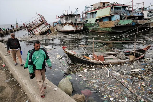 Residents walk past Jakarta's water front full of garbage, mainly plastic waste, at Muara Baru traditional seaport in Jakarta, Indonesia, on May 18, 2023. The Indonesian government set goals for itself in 2019, hoping to eliminate ocean trash by 70 percent by 2025. (Photo by Adi Weda/EPA/EFE/Rex Features/Shutterstock)