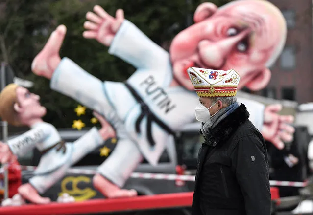 A reveller stands in front of a political carnival float depicting Russia's President Vladimir Putin fighting with opposition leader Alexei Navalny in the streets of Duesseldorf, Germany, Monday, February 15, 2021. Because of the coronavirus pandemic the traditional “Rosenmontag” carnival parade are canceled but eight floats are pulled through the empty streets in Duesseldorf, where normally hundreds of thousands of people would celebrate the street carnival. (Photo by Martin Meissner/AP Photo)