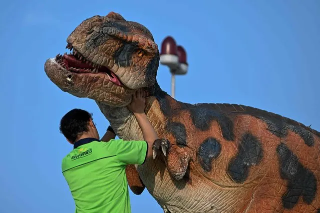 A worker adjusts a performer's dinosaur costume on the top of Penang state's landmark Komtar tower on Penang island in Malaysia on March 10, 2023. (Photo by Mohd Rasfan/AFP Photo)