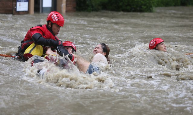 Firefighters use a rope to rescue a group of people stranded in a flooded street on July 12, 2018 in Chengdu, Sichuan Province of China. A strong storm has hit many parts of southwest China's Sichuan Province since Monday, causing landslides and floods in the region. (Photo by Wang Hongqiang/Chengdu Economic Daily/VCG)