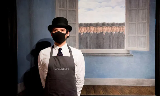A gallery worker stands alongside an artwork titled “Le mois des vendanges” by Rene Magritte during a photocall at Christies auction house in central London on March 16, 2021. (Photo by Ian West/PA Wire Press Association)