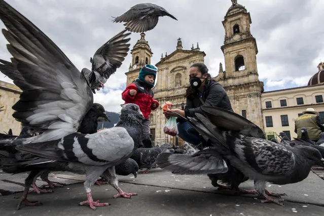A woman and her child feed pigeons while wearing a face mask at the Bolivar Square in Bogota, on February 23, 2021. (Photo by Juan Barreto/AFP Photo)