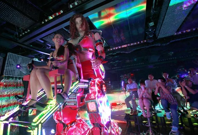 Bikini-clad women (L) sit as they operate a 3.6 metre-high custom-made female robot as customers take photos, at the “Robot Restaurant” in Kabukicho, one of Tokyo's best-known red light districts, August 16, 2012.  (Photo by Yuriko Nakao/Reuters)