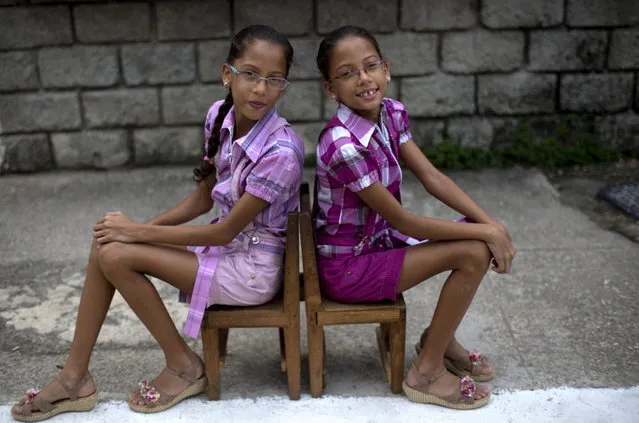 In this Sept. 29, 2013 photo, nine-year-old twin sisters Camila, left, and Carla Rodriguez pose for a portrait along their street in Havana, Cuba. 12 sets of twins live along two consecutive blocks in western Havana, ranging in age from newborns to senior citizens. “We love living on this block because we have twin friends”, said Carla. (Photo by Ramon Espinosa/AP Photo)