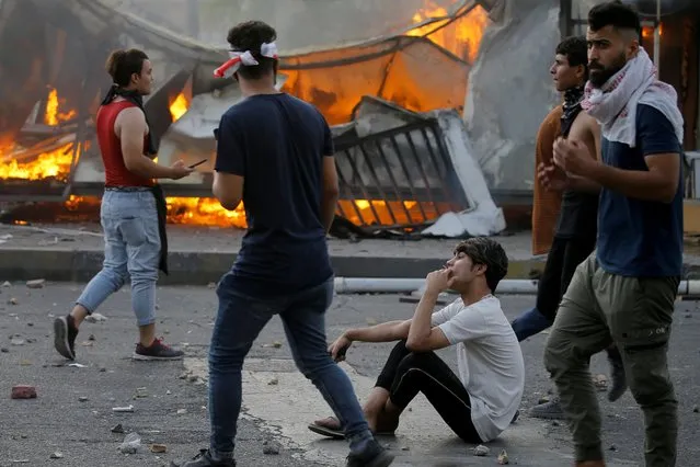 A demonstrator smokes a cigarette near a fire site during an anti-government protest in Baghdad, Iraq on May 25, 2021. Hundreds demonstrated in Tahrir Square, shouting slogans against Iran-backed militias and accusing Prime Minister Mustafa al-Kadhimi's government of failing to answer for the deaths of dozens of activists shot dead in different parts of Iraq in recent months. (Photo by Thaier Al-Sudani/Reuters)