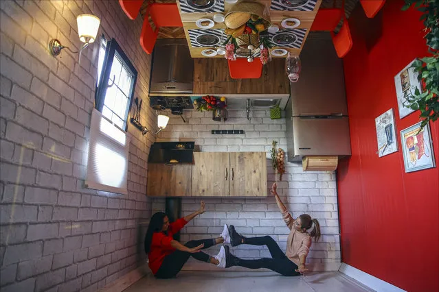 Two women sit inside the kitchen of an upside down house made of a truck trailer at a shopping center in Sultanbeyli district of Istanbul, Turkey on November 01, 2018. Realistic furnitures were used to design the upside down house such as curtains, kitchen furnitures, toilet, bedroom, wardrobes, sofa sets and a washing machine placed on the ceiling. (Photo by Serhat Çada/Anadolu Agency/Getty Images)