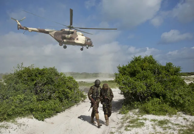 In this Wednesday, December 14, 2011 file photo, two Kenyan army soldiers shield themselves from the downdraft of a Kenyan air force helicopter as it flies away from their base near the seaside town of Bur Garbo, in Somalia. Residents in the town of in El-Ade in Somalia said Tuesday, January 26, 2016 that Kenyan forces have pulled out of the town in southwestern Somalia where Islamic extremists killed Kenyan peacekeepers recently. (Photo by Ben Curtis/AP Photo)