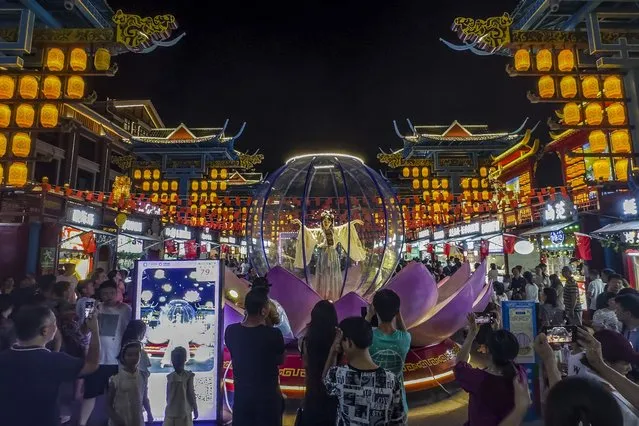 Visitors watch an artist perform in a new night market during a weeklong national holiday in Nanning in south China's Guangxi Zhuang Autonomous Region on September 30, 2023. Tourism in China bounced back to pre-pandemic levels during a recent eight-day national holiday, giving a temporary boost to the nation's flagging economy. (Photo by Chinatopix via AP Photo)