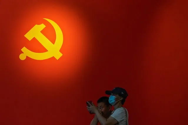 A woman wearing a face mask to help curb the spread of the coronavirus and a child stand near a Communist Party's flag on display at an exhibition promoting China's achievement under communist party from 1921 to 2021, in Beijing, Sunday, June 20, 2021. Authorities are gearing up to mark the 100th anniversary of the founding of China's ruling Communist Party, which will be observed on July 1. (Photo by Andy Wong/AP Photo)