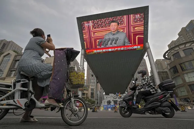 A woman on her electric-powered scooter films a large video screen outside a shopping mall showing Chinese President Xi Jinping speaking during an event to commemorate the 100th anniversary of China's Communist Party at Tiananmen Square in Beijing, Thursday, July 1, 2021. (Photo by Andy Wong/AP Photo)