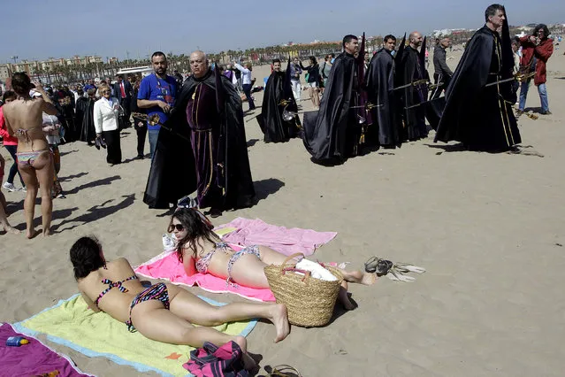 Penitents walk past beachgoers as they carry the statue of the Santisimo Cristo del Salvador (not pictured) during a procession to pray for those who died in the sea, on the beach in Valencia, April 3, 2015. Hundreds of Easter processions take place around the clock throughout Spain during Holy Week, drawing thousands of visitors. (Photo by Heino Kalis/Reuters)