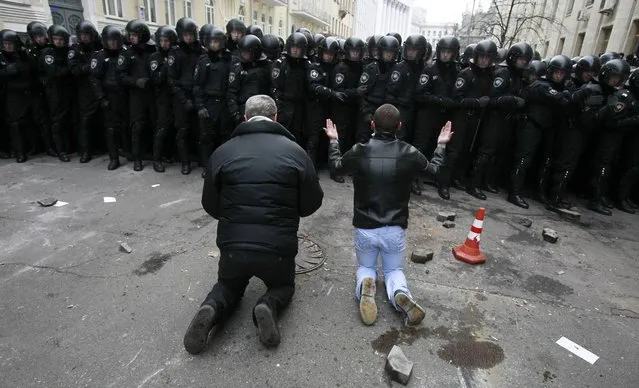 Men kneel down while riot police stand guard near the presidential administration building during a rally held by supporters of EU integration in Kiev, December 1, 2013. (Photo by Gleb Garanich/Reuters)