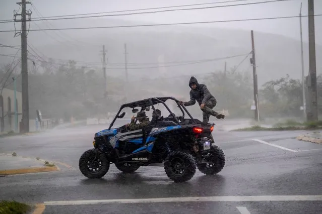 A man jumps into an all terrain vehicle as Hurricane Fiona made landfall in Ponce, Puerto Rico on September 18, 2022. (Photo by Ricardo Arduengo/Reuters)