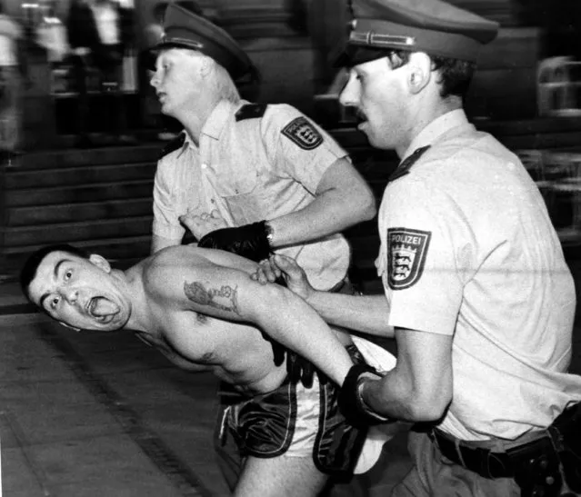 In this Sunday June 13, 1988 file photo West German police officers arrest an English soccer hooligan who sticks out his tongue. Rioting broke out between some 100 hooligans and the police in downtown Stuttgart, West Germany following the European Soccer Championships match between England and Ireland. England was defeated by Ireland 0-1. (Photo by Kraufmann/AP Photo/File)