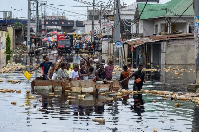 People cross the floodwater of the Carrigr's bridge in a pirogue in the Pompage district in Kinshasa on January 9, 2024 following heavy rains and the flood of the Congo River. (Photo by Arsene Mpiana/AFP Photo)