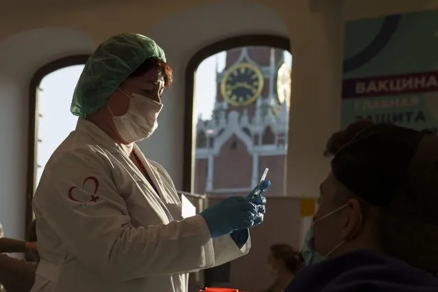 A medical worker prepares a shot of Russia's Sputnik Lite coronavirus vaccine at a vaccination center in the GUM, State Department store, in Red Square with the Spasskaya Tower in the background, in Moscow, Russia, Tuesday, October 26, 2021. The daily number of COVID-19 deaths in Russia hit another high Tuesday amid a surge in infections that forced the Kremlin to order most Russians to stay off work starting this week. (Photo by Pavel Golovkin/AP Photo)